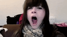 a woman is yawning with her mouth open while wearing a scarf .