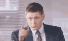 a man in a suit and tie is pointing his finger at the camera .
