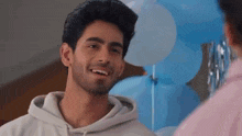 a man in a hoodie is smiling and looking at another man in front of blue balloons .
