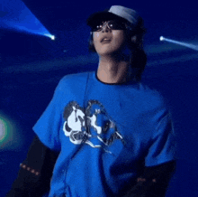 a man wearing a hat and sunglasses is wearing a blue shirt with a mickey mouse on it .