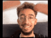 a young man with glasses and a beard is smiling and looking at the camera .