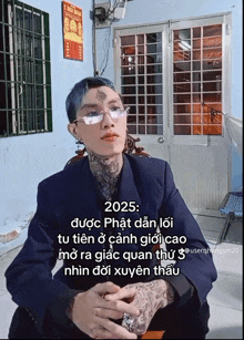 a man with glasses and a tattoo on his forehead is sitting in front of a door with a sign that says 2025