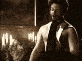 a man without a shirt is standing in a dark room with candles