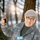 an elderly man holds up a cup of coffee in front of a tree in a forest