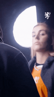 a woman in an orange shirt is standing in front of a white light .