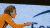 a man in an orange shirt is pointing at a sign
