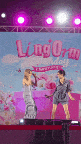 two women singing in front of a sign that says lingorm birthday charity 2022