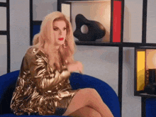 a woman in a gold dress is sitting on a blue chair in a room .