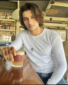 a man in a white shirt sits at a bar with a drink in his hand