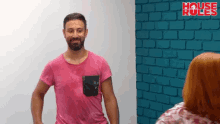 a man in a pink shirt stands in front of a blue brick wall with the words house rules written on it