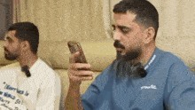 a man with a beard is looking at his cell phone while sitting on a couch .
