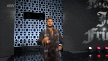 a man in a plaid jacket and scarf is giving a thumbs up in front of a screen with aew written on it