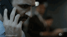 a man talking on a cell phone with #theblacklist on the bottom right