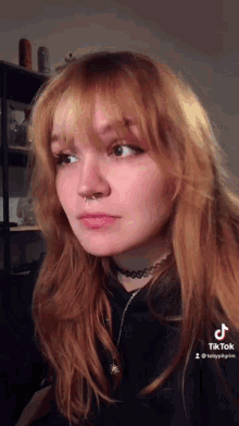 a woman with red hair and a nose ring is wearing a choker and a black shirt .