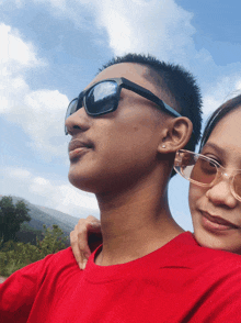 a man wearing sunglasses and a woman wearing glasses look up at the sky