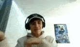 a young man wearing headphones and a hat is standing in front of a creeper poster on the wall .