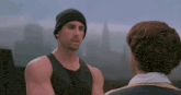 a man in a black tank top is talking to another man in a white shirt
