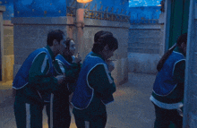 a group of people wearing blue vests and green pants are standing in a dark room