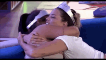 a woman wearing a crown is hugging another woman who is wearing a white shirt