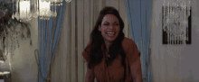 a woman is laughing in a living room with a chandelier behind her .