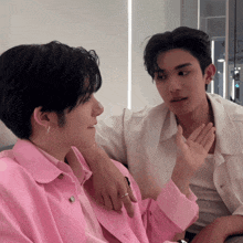 two young men are sitting next to each other and one is wearing a pink jacket