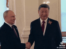 two men in suits and ties shaking hands in a room .