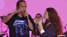 a man in a metallica shirt sings into a microphone while a woman looks on