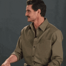 a man with a mustache is wearing a green shirt and talking into a microphone .