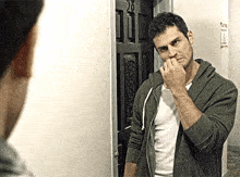 a man is looking at himself in a mirror while wearing a hoodie and a white shirt .