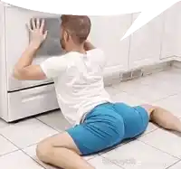 a man in blue shorts is kneeling on the floor reaching into an oven .