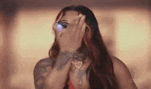 a woman is covering her face with her hand while wearing glasses .