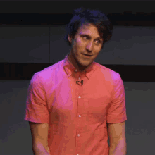 a man wearing a pink shirt has a microphone on his shirt