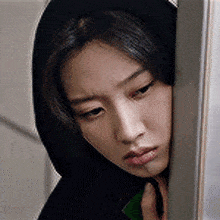 a woman in a black hoodie is leaning against a wall and looking down .