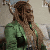 a woman in a green jacket sits on a couch in front of a wall that says sistas