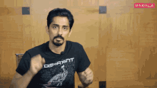 a man wearing a black shirt that says discreet holds his fist up