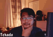 a man wearing glasses and a headset is sitting in front of a screen that says tekada