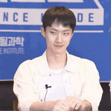 a young man in a white shirt is sitting at a table with a microphone .