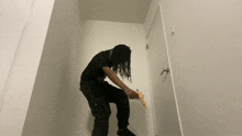a man with dreadlocks is kneeling down in front of a white wall