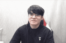 a man wearing glasses and a black shirt is sitting in front of a white curtain