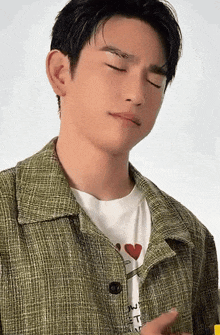 a young man wearing a green jacket and a white shirt with a heart on it is making a funny face .