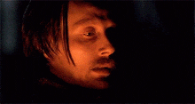 a close up of a man 's face with a snake around his neck in a dark room .