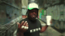 a man wearing a hat that says tata holds a cup