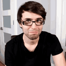 a man wearing glasses and a black shirt looks at the camera