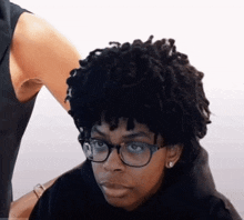 a woman with dreadlocks and glasses is getting her hair cut by a hairdresser .
