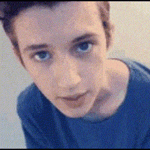 a young man in a blue shirt is looking at the camera