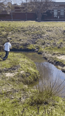 a boy is walking along a stream in front of a building that says great bridge elementary school