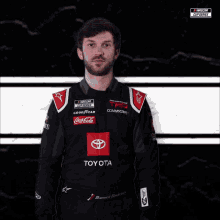 a man wearing a toyota racing suit stands in front of a nascar logo