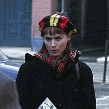 a woman wearing a plaid hat and scarf is walking down the street
