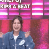 a woman in a denim jacket is laughing in front of a pink background that says kips a beat .