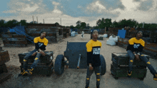 a man wearing a yellow shirt that says celin pari sits on a box